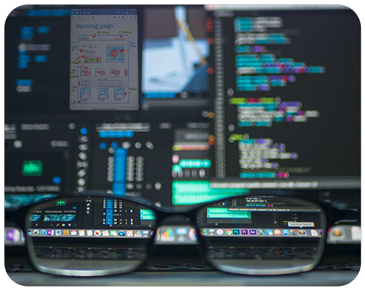 glasses on a desk in front of computer code on a monitor